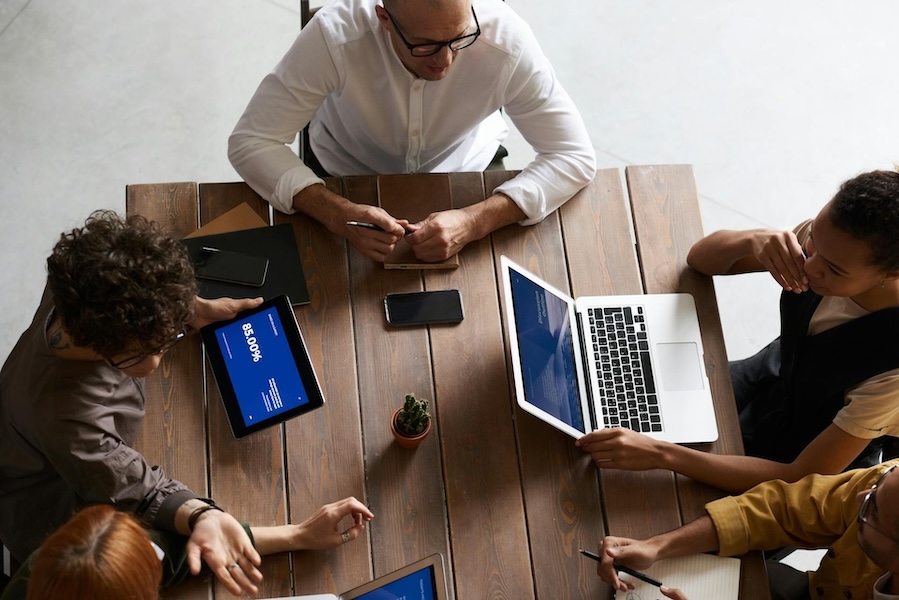 Plusieurs personnes sont assises autour d'une table avec des ordinateurs portatifs et des cahiers déposés dessus.